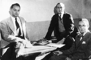 Robert Manners, Assistant Professor of Anthropology and Phillip Rieff, Instructor in Social Relations Lewis Coser, Lecturer in Social Sciences, seated around a table with various papers.