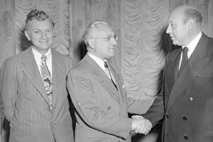 President Abram Sachar and Rabbi Israel Goldstein shake hands with George Alpert stands to Sachar's right.