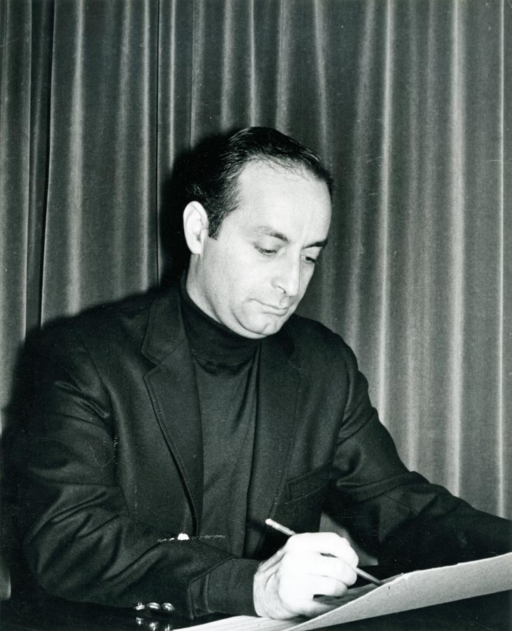 Seated man in front of curtain, writing