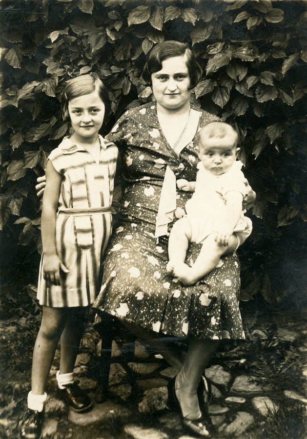 Sitting woman holding baby with right arm, left arm wrapped around a standing young girl