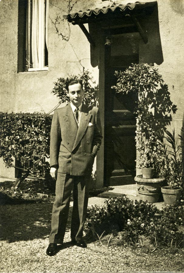 Young man in suit, standing in front of a house