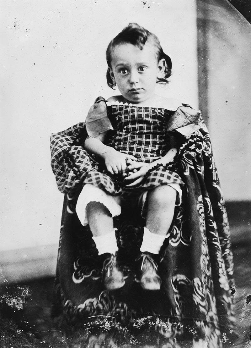 A 2 year old Louis Brandeis seated with tall white socks, lace up shoes, and a large fabric covering (black and white photograph, 1858)