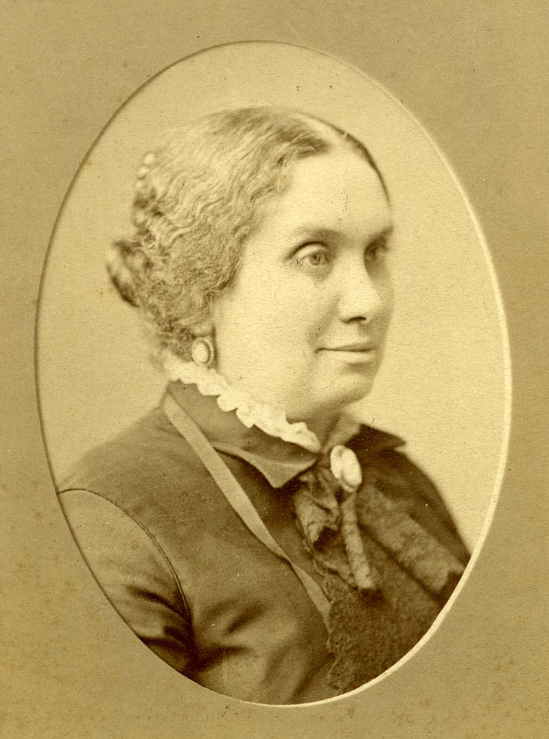 A sepia-tinted photograph of Frederika Dembitz looking into the distance with a dark ensemble and her hair up in a bun.