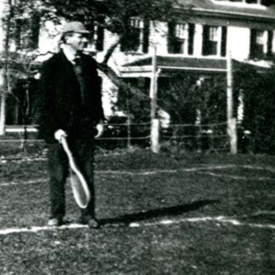 Louis D. Brandeis standing at the edge of a tennis court as he holds a racket