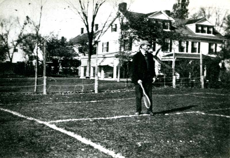 Louis D. Brandeis standing at the edge of a tennis court holding a racket