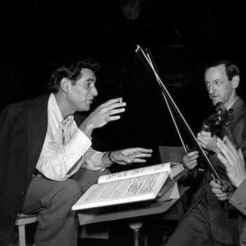 Bernstein speaking at the symposium, with a violinist standing beside him.