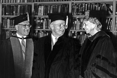 President Sachar, President Truman, & Eleanor Roosevelt, in academic regalia, standing in front of a wall filled with books.