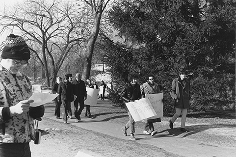 White students holding paper signs and walking in a line around a building; text of sign: We Support Afro Demands.
