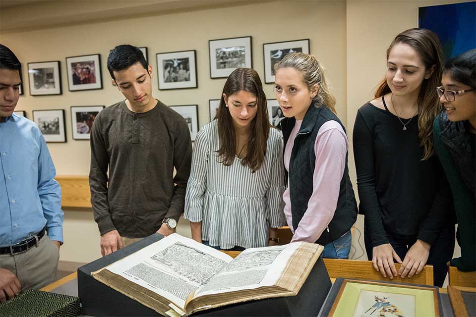 Students look at a large open book on a table