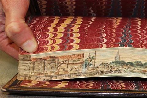 Colorful fore-edge painting of a beach town with a port docking boats