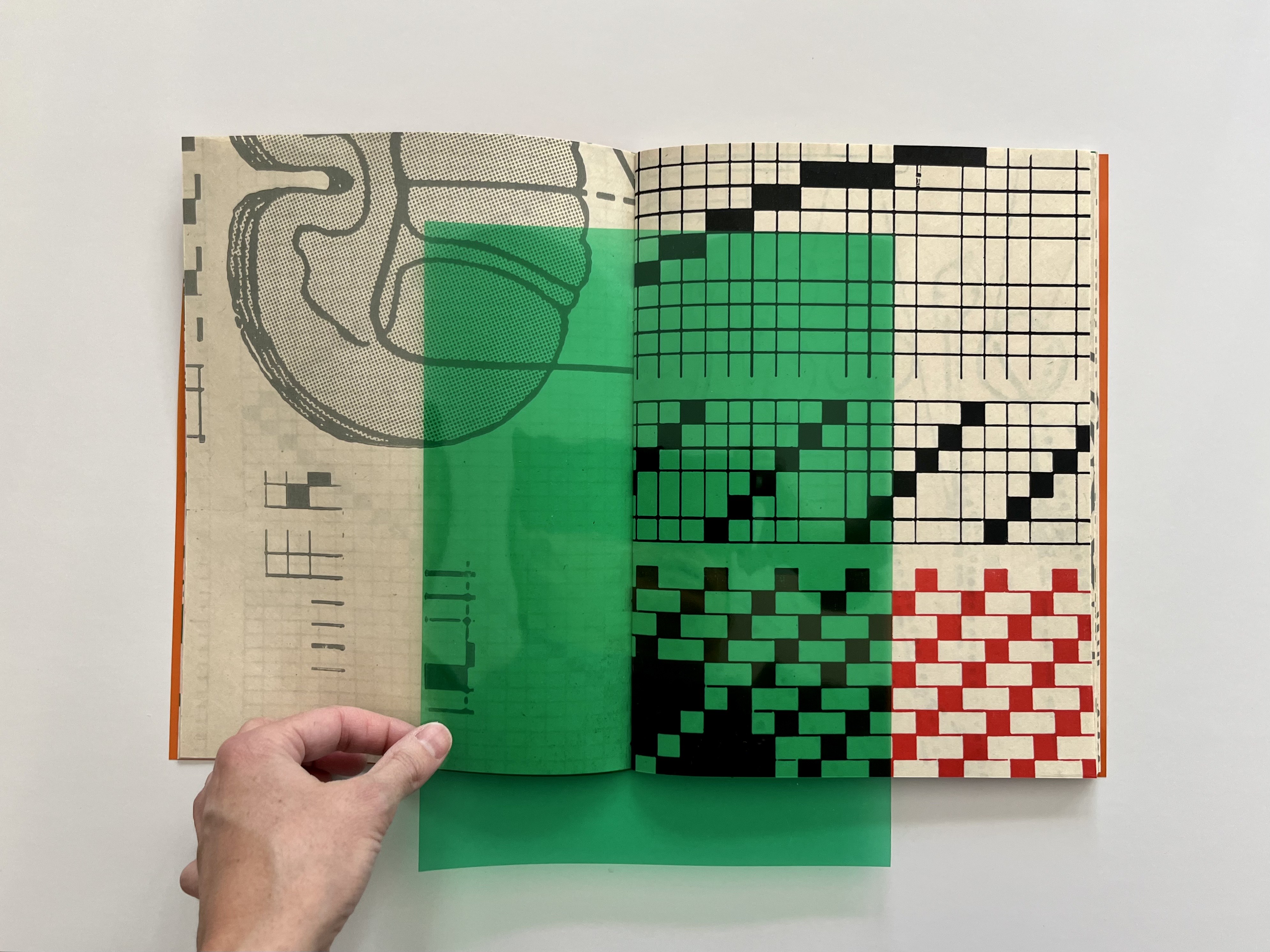 Image of a book with geometric designs and green sheet of paper on top. 