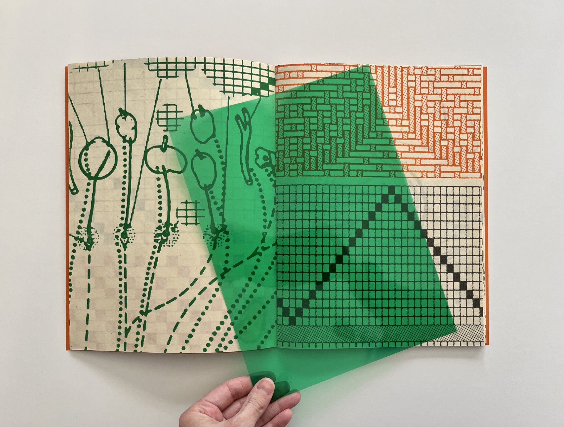 Image of a book with geometric designs and green sheet of paper on top. 