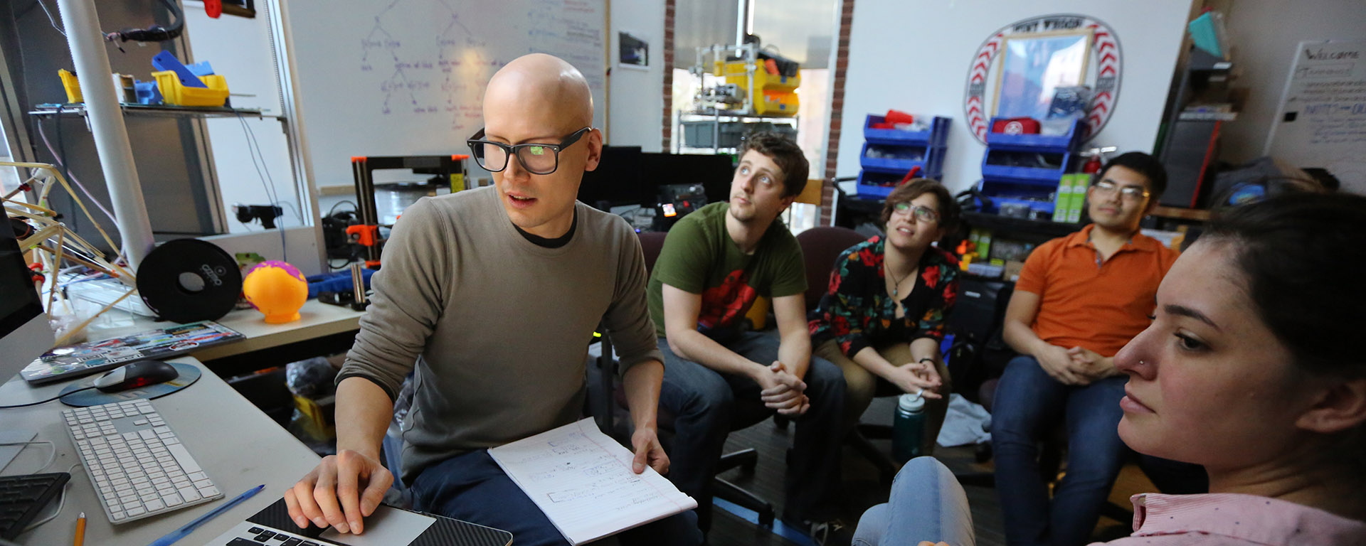 The Research Technology and Innovation Team gathers around a computer for a meeting in the Brandeis Makerlab