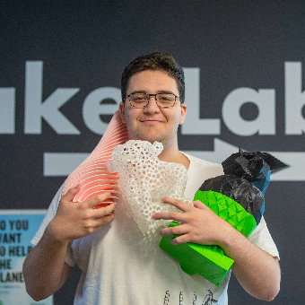Harrison holding up three 3D printed objects, a large translucent lion with many holes, a green and black owl, and  an orange and white vase.