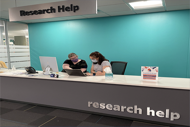 A librarian helps a patron at the Research Help desk