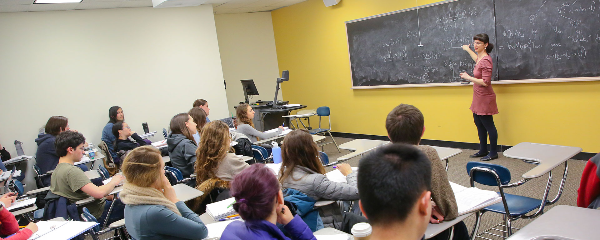 Sophia Malamud stands at a blackboard and teaches a classroom full of students.