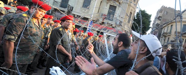 Egyptian soldiers stand guard behind barbed wire as protesters demonstrate outside the defense ministry, headquarters of the Supreme Council of the Armed Forces in Cairo.