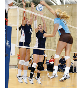 Becca Fischer, center, blocks a Tufts spiker in a Brandeis home game.