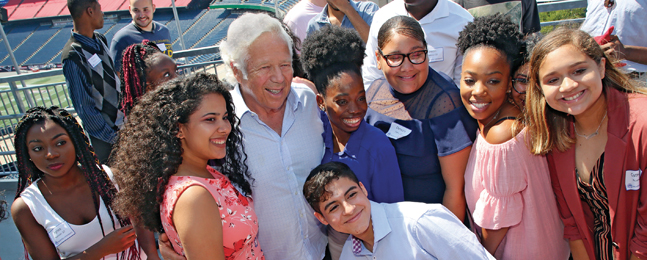 Robert Kraft standing with a group of smiling students.