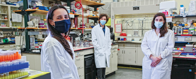 Photo of three people wearing face masks, standing in a laboratory