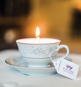Photo of a lit candle in a delicate gold-rimmed cup and saucer.