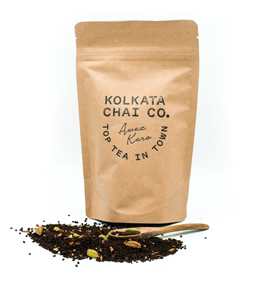 Photo of a mound of loose tea, a small wooded spoon and a brown bag printed with the words "Kolkata Chai Co., Awaz Kara, Top Tea in Town."