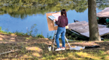 A student standing at an easel paints outside on a sunny day.