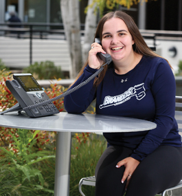 Photo of Diana Epstein, sitting at a table outside talking on a phone.