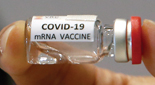 Close-up of a small vial of clear liquid labeled "COVID-19 mRNA Vaccine" held between a thumb and forefinger.