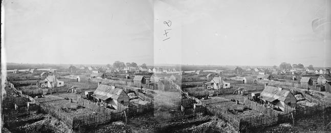 A 19th-century black-and-white photo of a refugee camp, with many shacks and houses scattered throughout a large parcel of land.