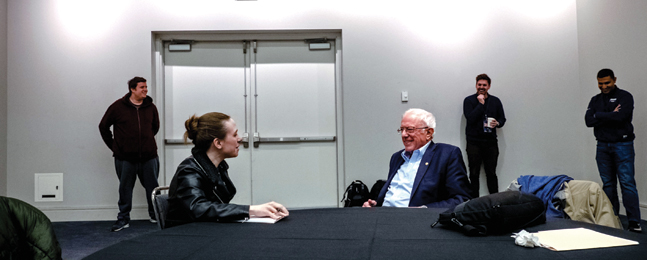Bruenig sits at a table and talks with a smiling Bernie Sanders.