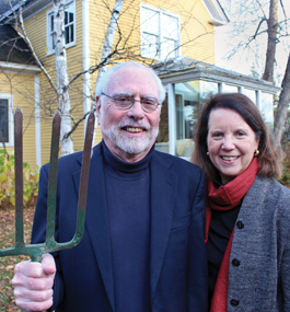 In what looks like homage to "American Gothic," a smiling man with a white beard and white hair holds an upright pitchfork, standing next to a smiling woman.