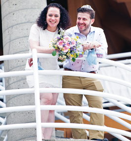 A smiling woman and man stand on a balcony with white railings.