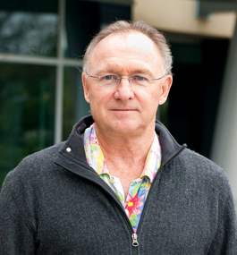 Head shot of a man in a colorful shirt and a dark-gray zipped sweater.