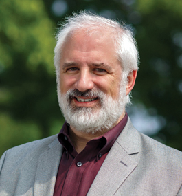 Head shot of a smiling man with white-gray hair and beard.