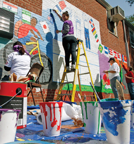 Young people paint a colorful mural on an external brick wall.