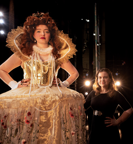 Photo of a woman in elaborate Elizabethan-style dress and jewels with a woman in a belted black dress