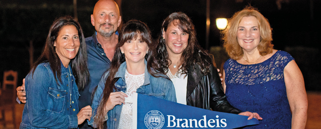 Photo of four women and a man posing with a blue Brandeis pennant 