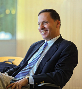 Photo of a smiling man leaning back in his chair and looking to his right 