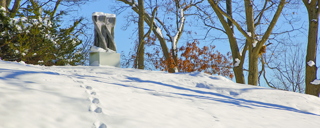 A photo of footsteps leading up a snowy hill; at the top is a snow-covered abstract metal sculpture.