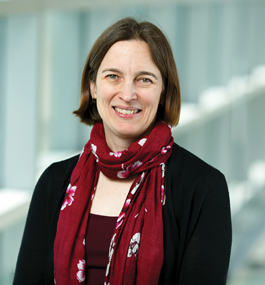 A woman with a brown bob and a maroon scarf around her neck smiles at the camera