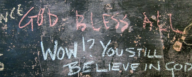 Photo of blackboard with the handwritten words "God Bless All" followed by "Wow!? You still believe in God."

