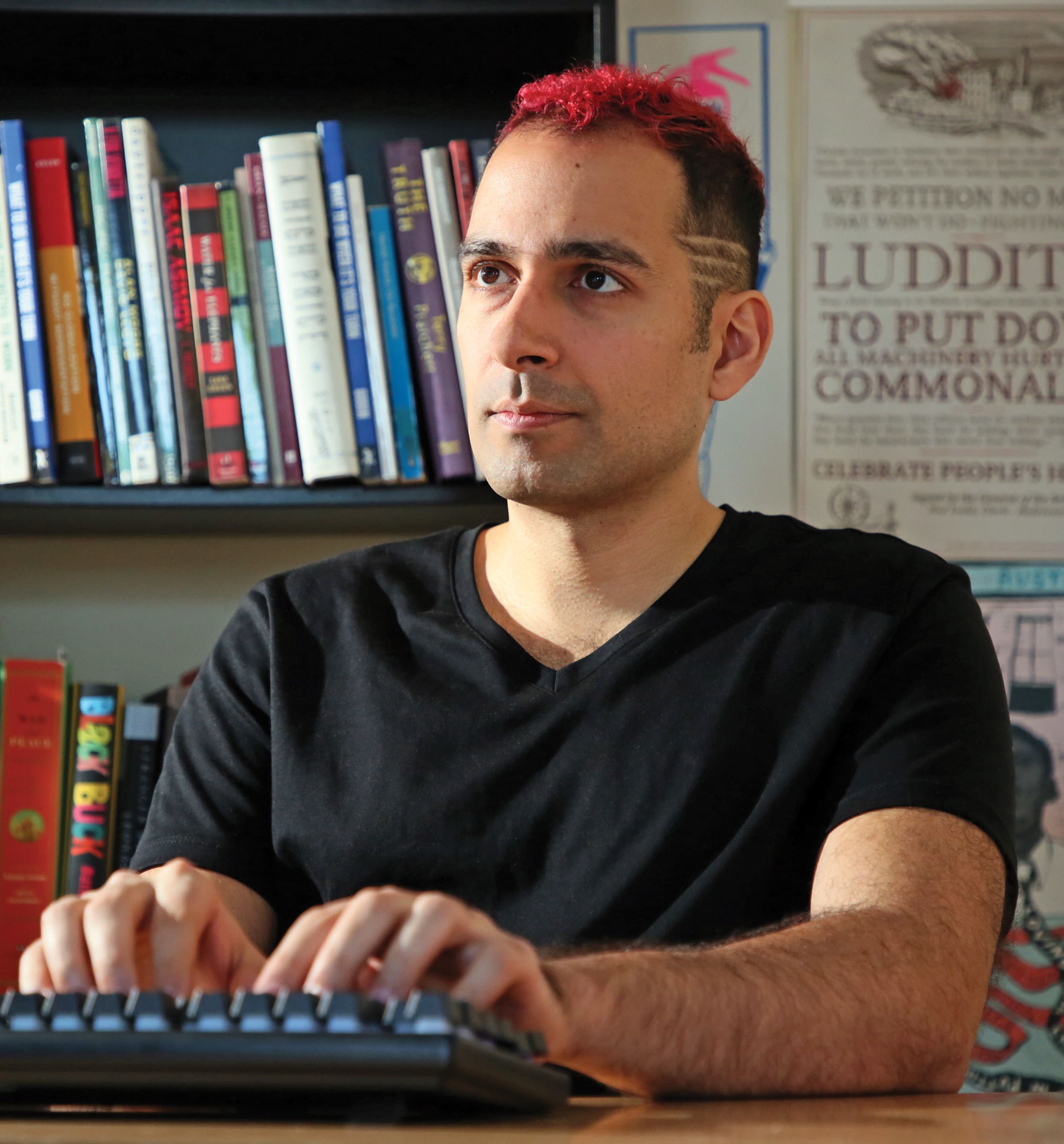 Massachi, wearing a back T-shirt, works at his keyboard with a shelf of books behind him.