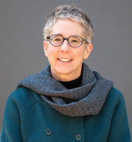 A woman with short gray-hair in a dark-gray sweater smiles for the camera.