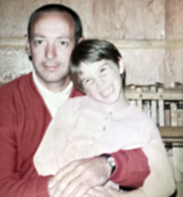 A faded color photo of a man in a red sweater holding a smiling little girl on his lap 