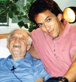 Smiling older man in blue shirt reclines next to seated younger man with dark hair