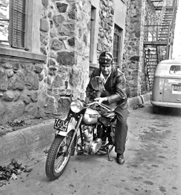 Black-and-white photo of a man on a motorcycle holding a dog