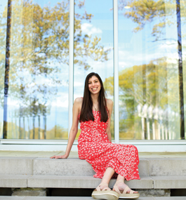 Photo of a smiling woman with long dark hair seated outside.