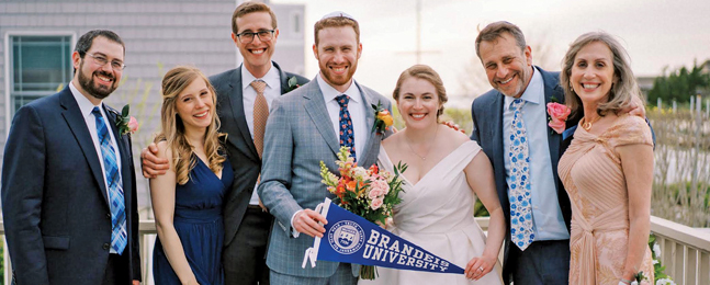 A bride and groom hold a blue Brandeis pennant surrounded by two women and three men