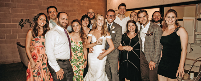 A bride and groom smile for the camera surrounded by a small group of people